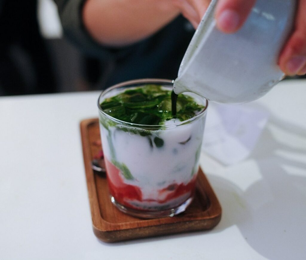 A 12oz iced matcha latte with strawberry, milk being poured over ice