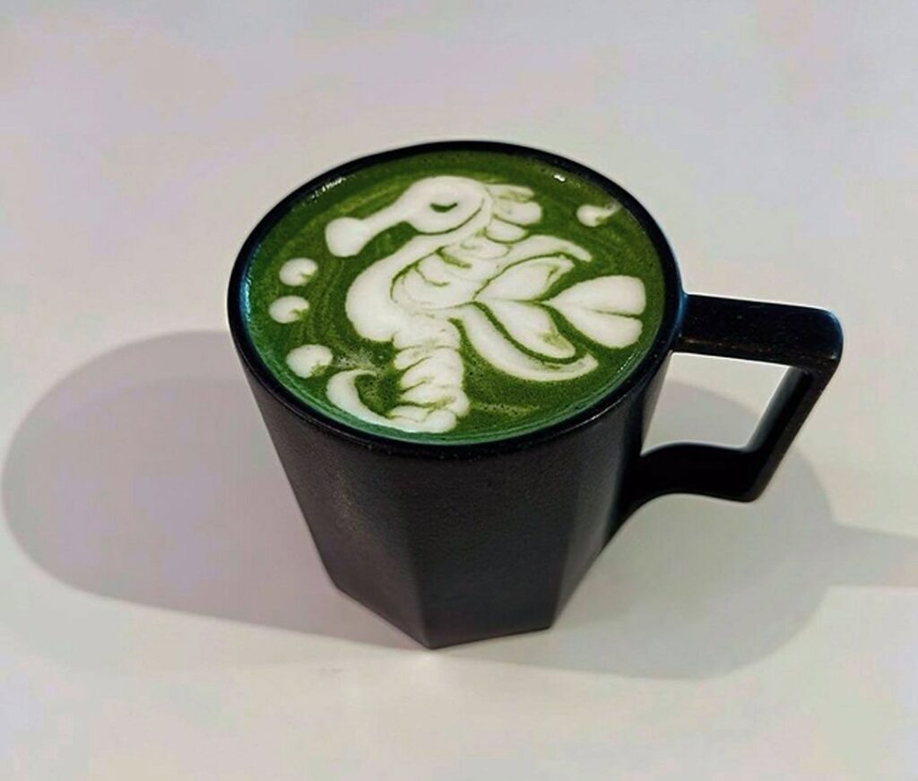 A 6oz hot matcha latte in a black cup with seahorse latte art